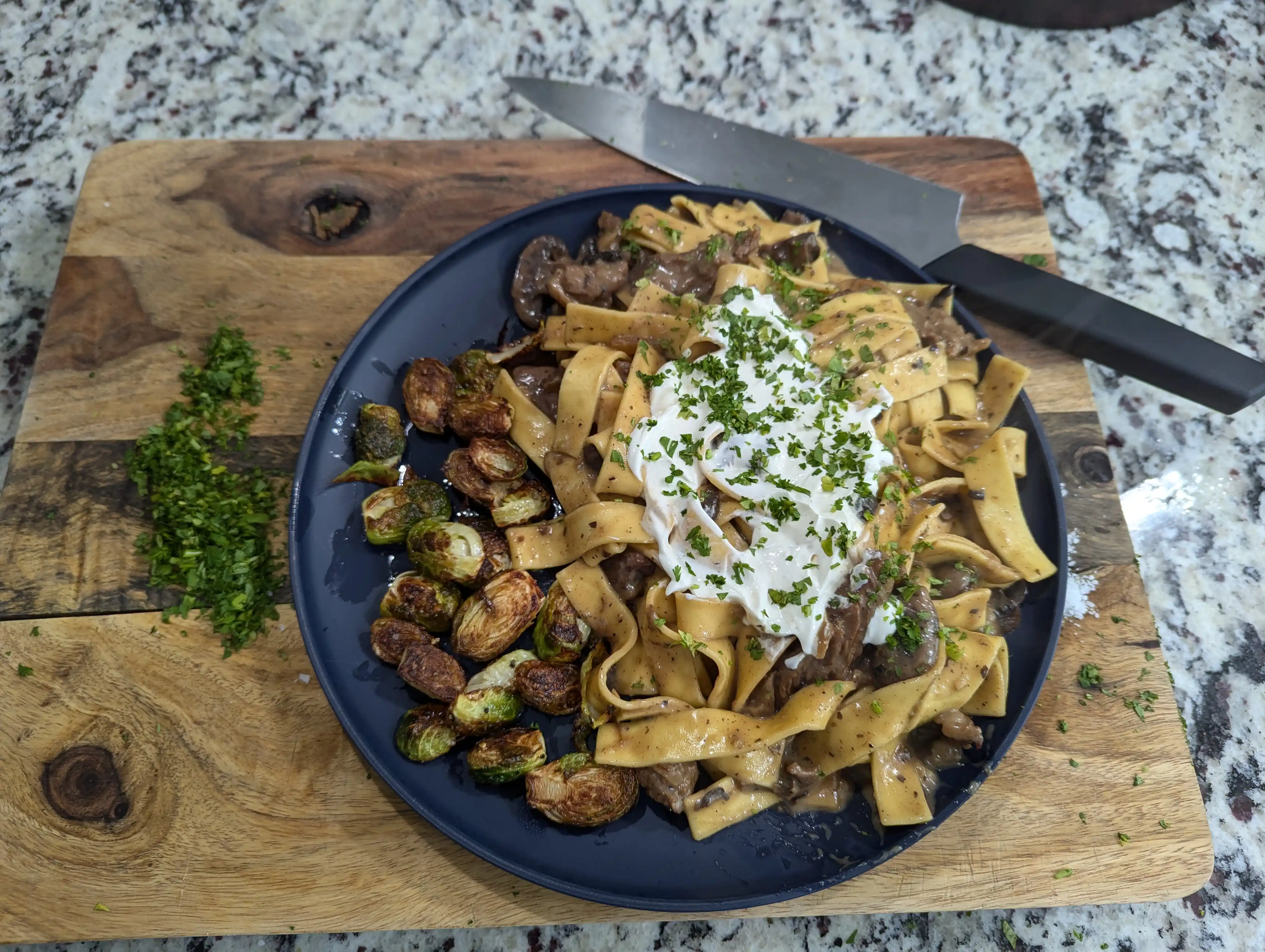 Beef Stroganoff served on noodles, garnished with parsley and sour cream, served with brussels sprouts