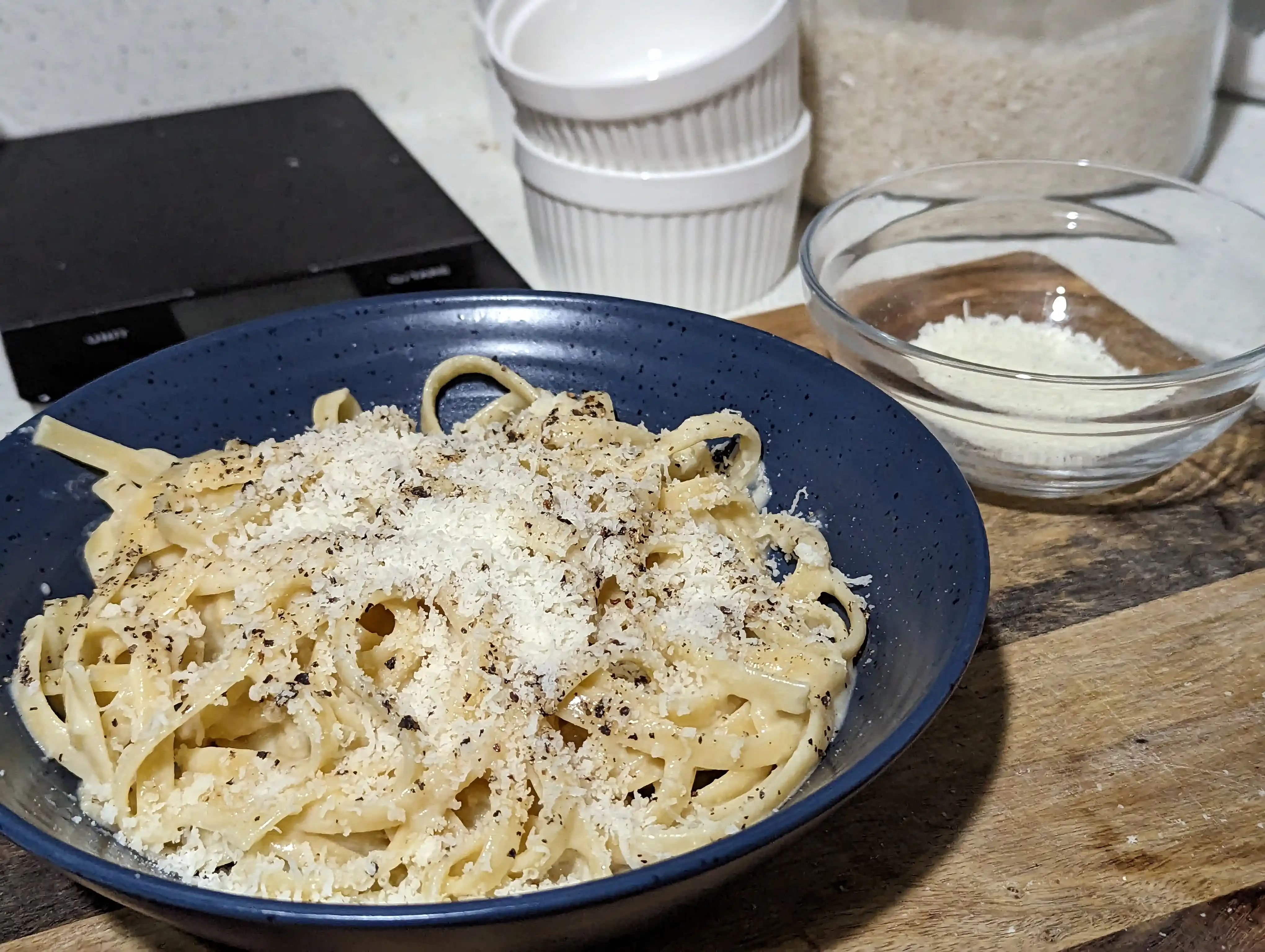 Bowl of fettuccine al burro garnished with additional pecorino romano and black pepper