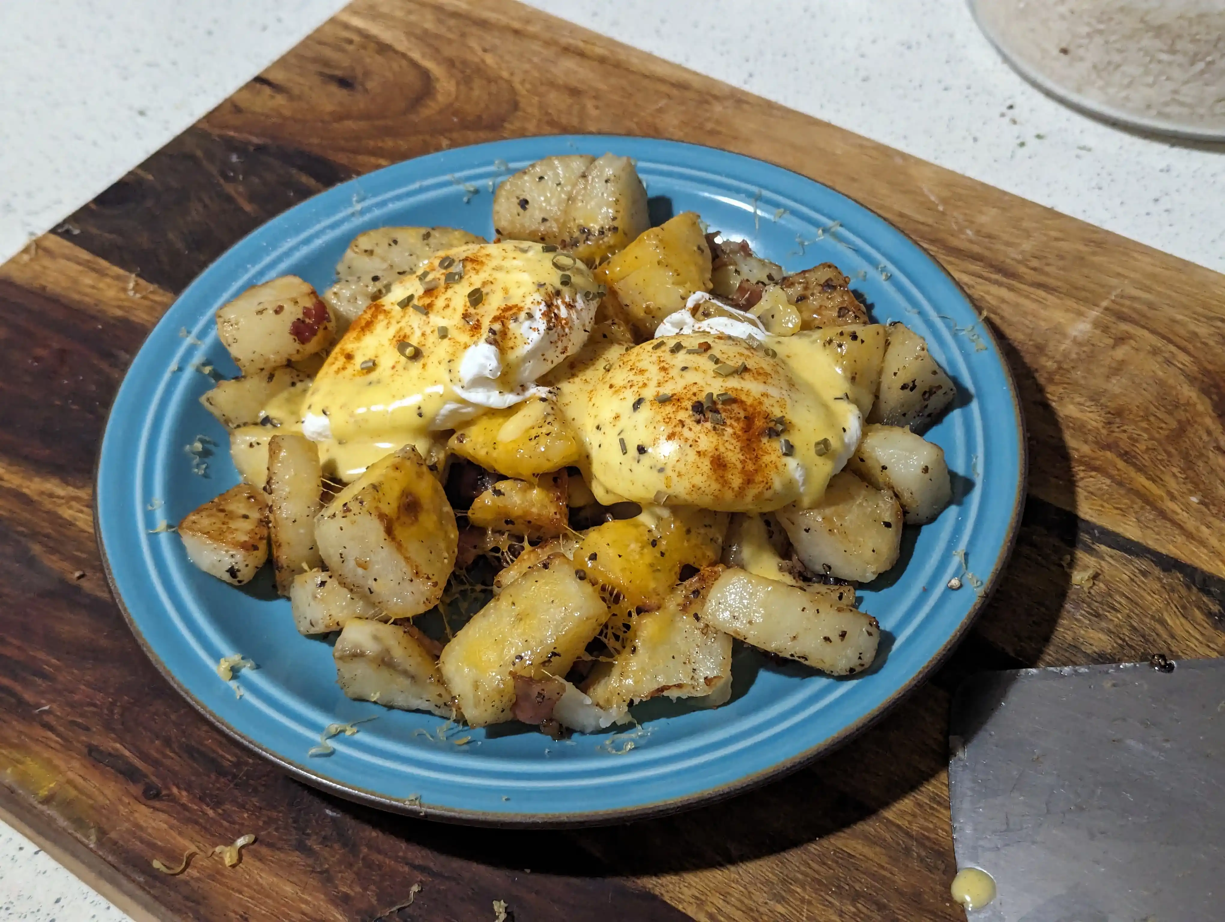 Roasted potatoes topped with cheddar cheese, poached eggs, hollandaise, cayenne pepper, and chives
